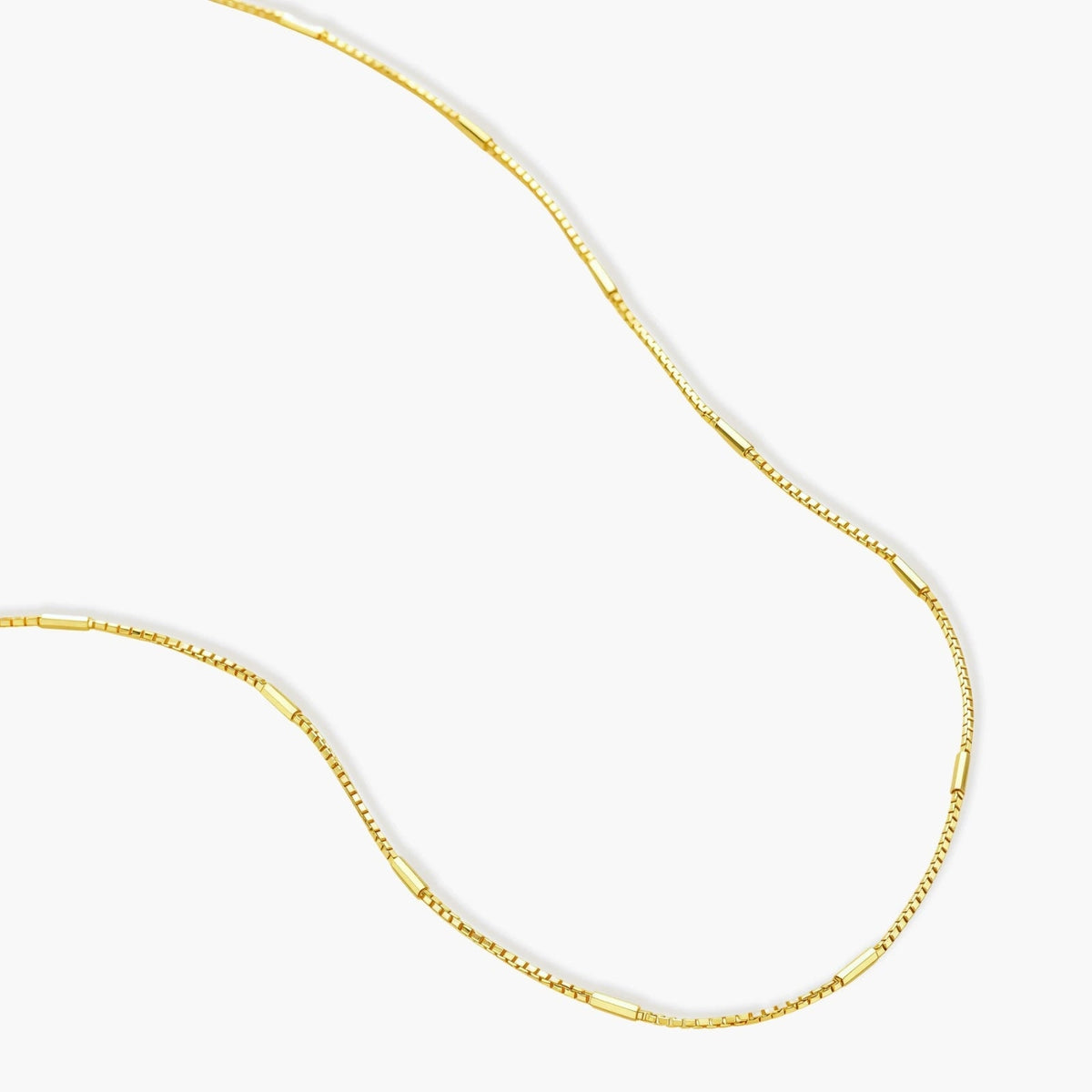 Delicate 14K gold-plated box chain necklace with evenly spaced bar links, shown flat on cream background.