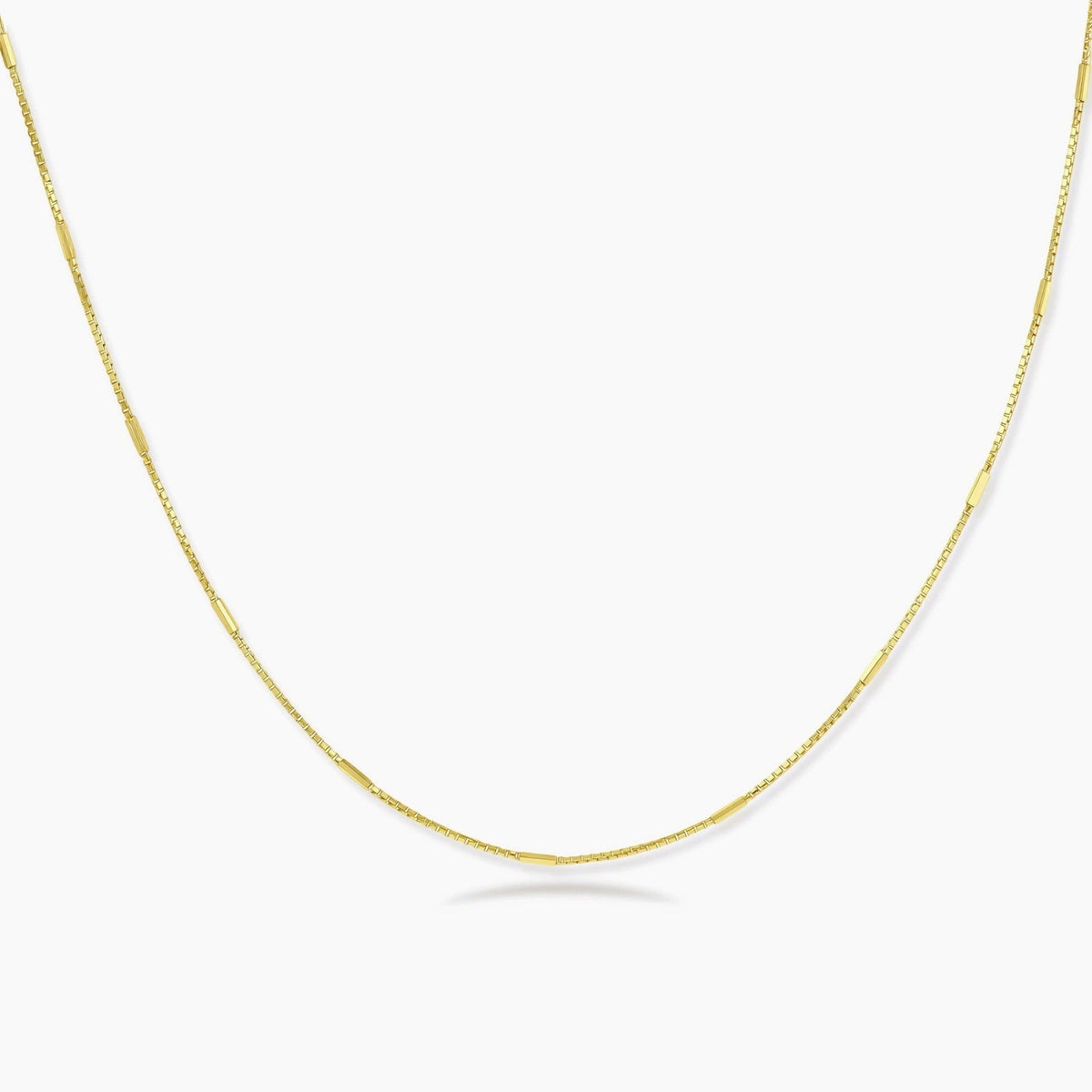Delicate 14K gold-plated box chain necklace with evenly spaced bar links, shown flat on cream background.